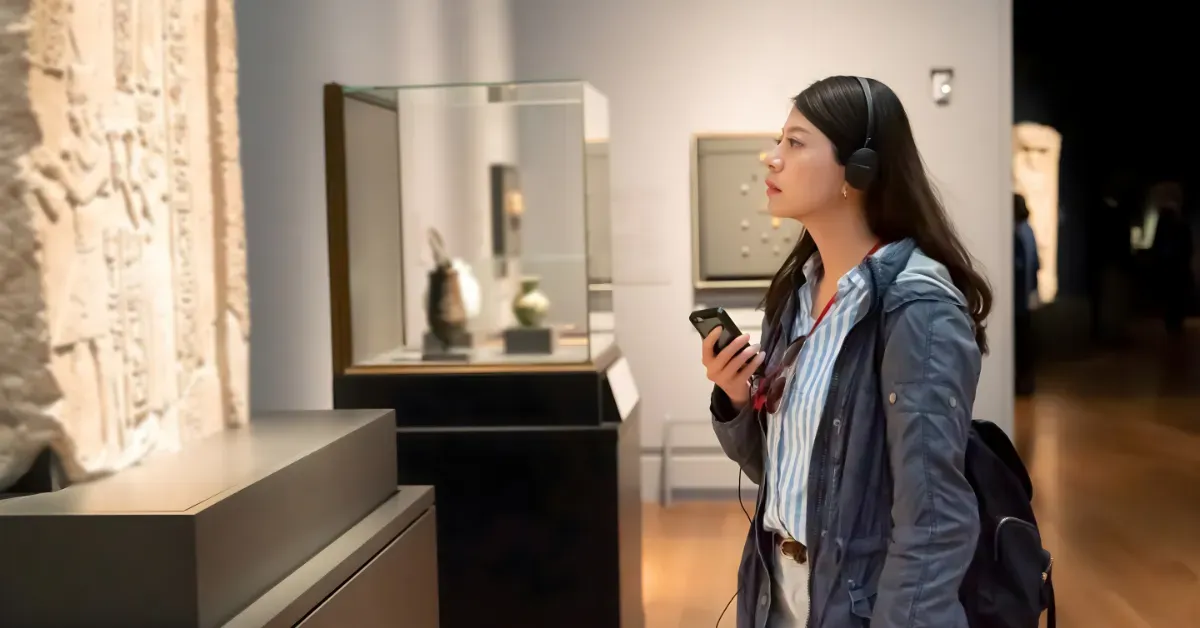 A woman wearing headphones taking a self-guided tour of an ancient stone relief exhibition in a museum.