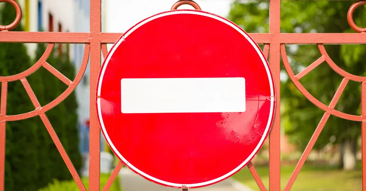 A circular red regulatory 'No Entry' sign with a white horizontal bar, mounted on an orange metal gate to indicate restricted access.