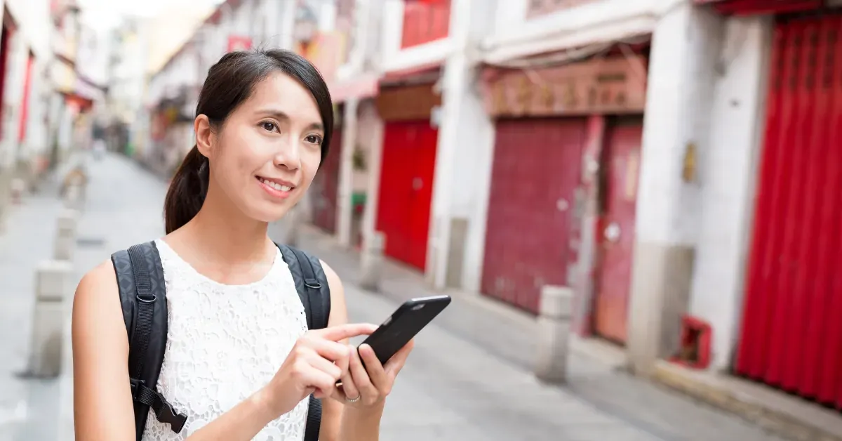 Woman using smartphone while exploring a city street using a self-guided tour app.